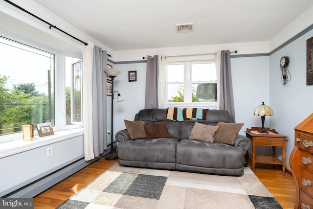 living room with a baseboard heating unit, light wood-style flooring, and visible vents