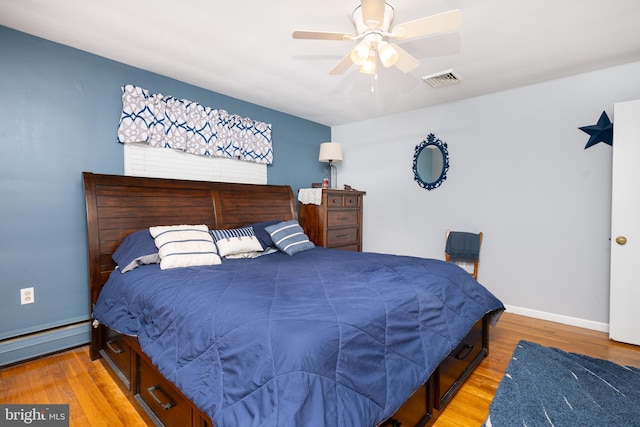 bedroom featuring visible vents, baseboards, baseboard heating, light wood-type flooring, and a ceiling fan
