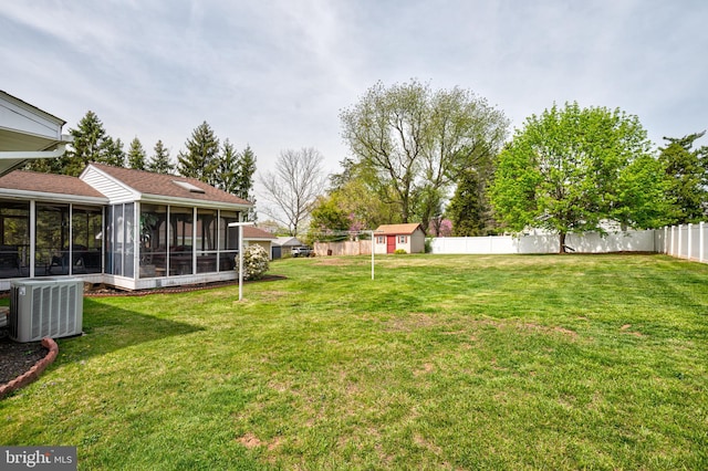 view of yard with a sunroom, central AC, an outdoor structure, a fenced backyard, and a shed