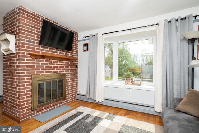 unfurnished living room featuring a brick fireplace, a baseboard heating unit, and wood finished floors