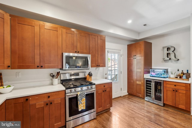 kitchen featuring beverage cooler, light countertops, brown cabinets, light wood-style flooring, and stainless steel appliances