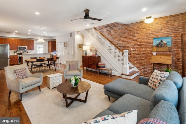 living area featuring brick wall, stairs, and light wood-style flooring