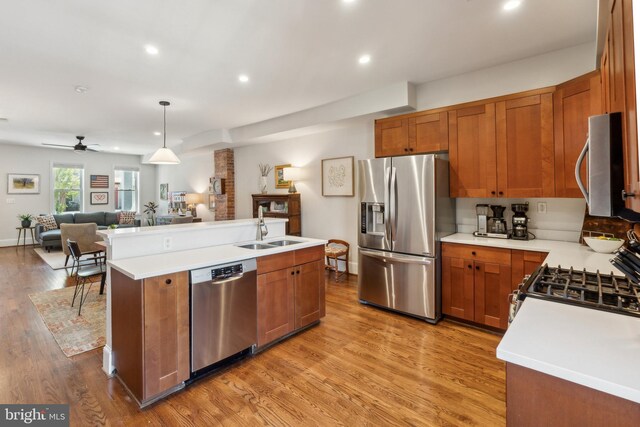 kitchen with light wood-style floors, open floor plan, brown cabinetry, and appliances with stainless steel finishes