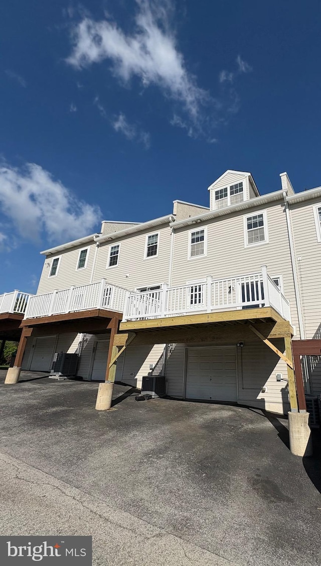 back of property with a deck, aphalt driveway, and a garage