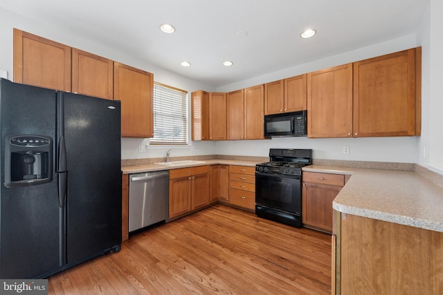 kitchen with a sink, light wood-type flooring, black appliances, light countertops, and recessed lighting