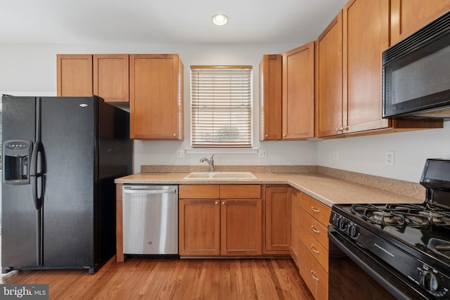 kitchen featuring recessed lighting, light wood finished floors, a sink, black appliances, and light countertops