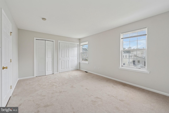 unfurnished bedroom with multiple windows, baseboards, multiple closets, and carpet floors