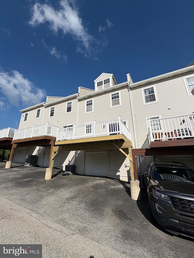 back of property with an attached garage, central AC unit, a wooden deck, and aphalt driveway