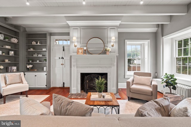 living area featuring beamed ceiling, wood finished floors, a fireplace, track lighting, and radiator
