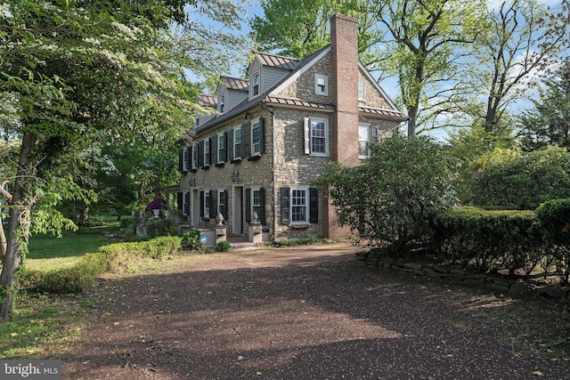view of front of house featuring a standing seam roof, metal roof, a chimney, and stone siding