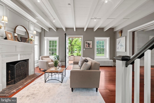 living room with radiator heating unit, wood finished floors, a fireplace, a ceiling fan, and beamed ceiling