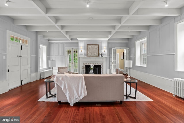 living area featuring radiator heating unit, dark wood-style floors, a premium fireplace, a decorative wall, and coffered ceiling