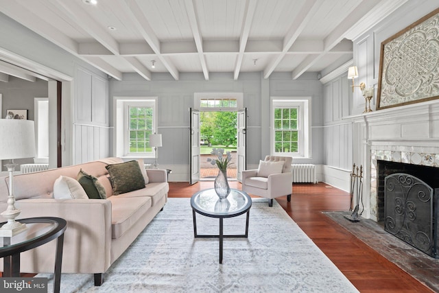 living area featuring radiator heating unit, wood finished floors, beamed ceiling, a fireplace, and a decorative wall