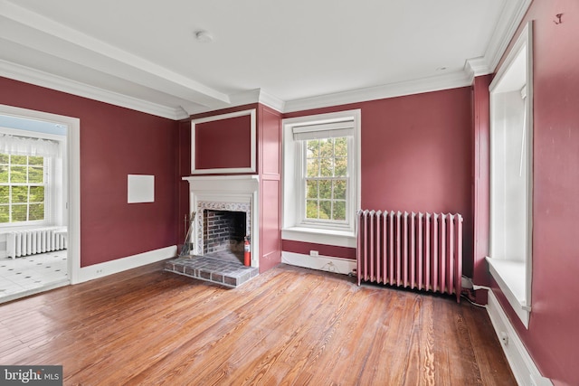 unfurnished living room featuring radiator, wood finished floors, a fireplace with raised hearth, ornamental molding, and baseboards