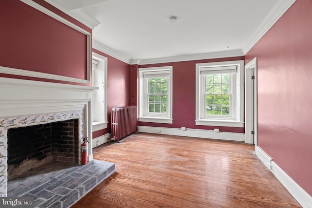 unfurnished living room with radiator heating unit, a premium fireplace, light wood-type flooring, crown molding, and baseboards