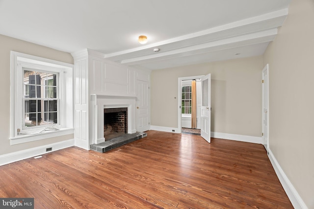 unfurnished living room with a fireplace with raised hearth, wood finished floors, baseboards, and beamed ceiling