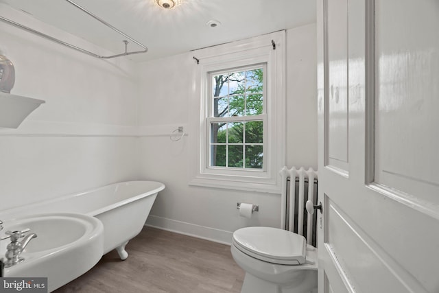 full bath with radiator heating unit, baseboards, toilet, wood finished floors, and a freestanding tub