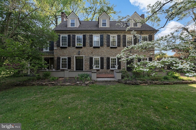 view of front facade with a front yard, a chimney, and stone siding