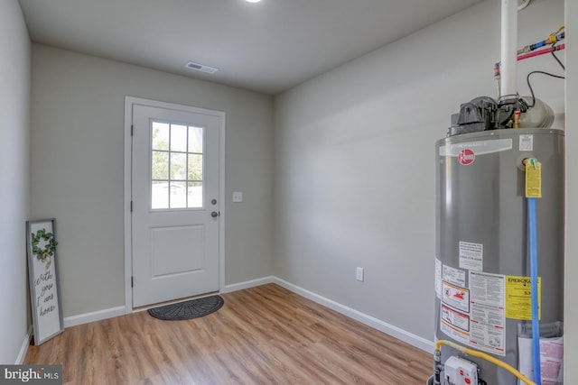 doorway to outside with baseboards, gas water heater, wood finished floors, and visible vents