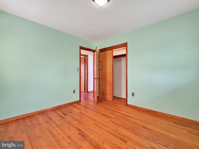unfurnished bedroom featuring light wood-type flooring, baseboards, and a closet