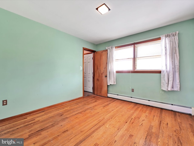 empty room featuring light wood-style floors, baseboards, and a baseboard heating unit