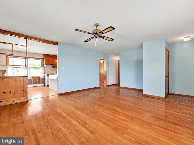 unfurnished living room with light wood-style floors, baseboards, ceiling fan, and arched walkways