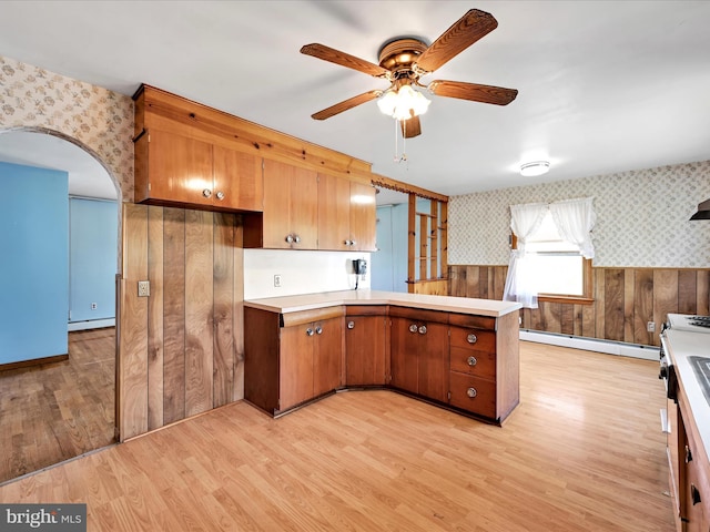 kitchen featuring light wood-style floors, a peninsula, a baseboard heating unit, and wallpapered walls
