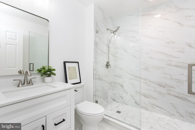 bathroom featuring toilet, a marble finish shower, and vanity