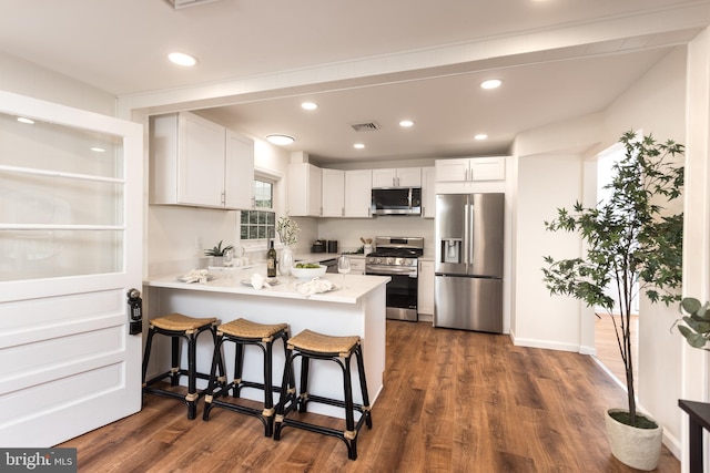 kitchen with white cabinets, visible vents, stainless steel appliances, dark wood finished floors, and a peninsula