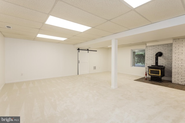 basement with a wood stove, a barn door, carpet, baseboards, and a drop ceiling