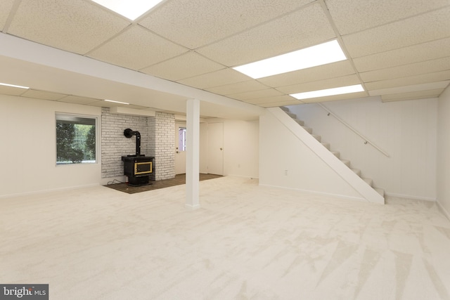 basement featuring a wood stove, stairway, carpet, baseboards, and a drop ceiling