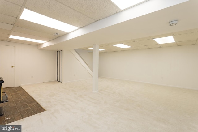 finished below grade area with dark colored carpet, stairway, a drop ceiling, and a wood stove