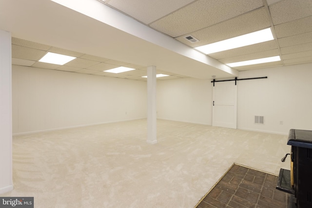 finished basement with carpet, a paneled ceiling, visible vents, and a barn door