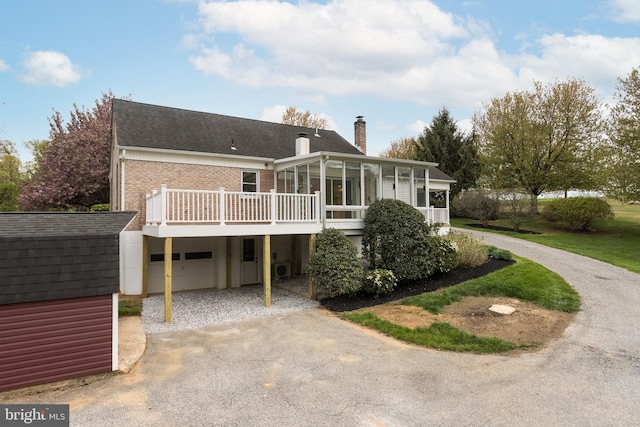 view of front of home featuring driveway, a chimney, a sunroom, brick siding, and a garage