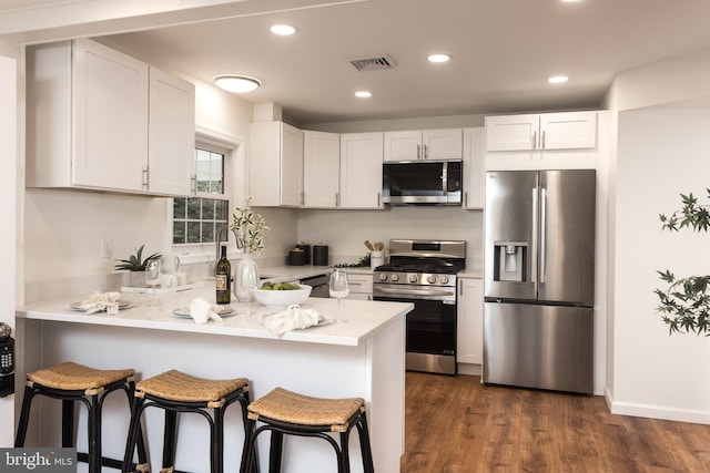 kitchen featuring dark wood-style floors, a peninsula, white cabinets, and appliances with stainless steel finishes