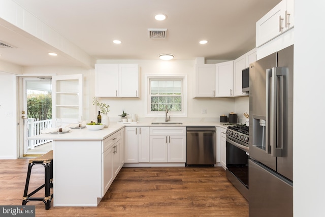 kitchen with a sink, visible vents, a peninsula, white cabinetry, and appliances with stainless steel finishes
