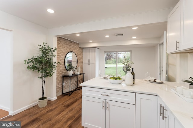 kitchen with white cabinetry, visible vents, brick wall, dark wood-type flooring, and a peninsula