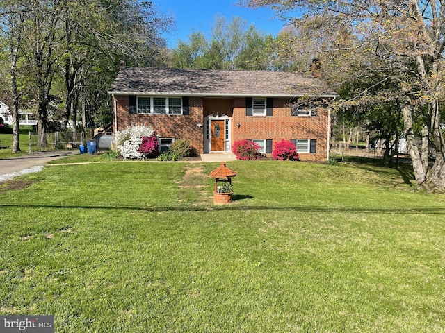 bi-level home with brick siding, fence, a chimney, and a front yard