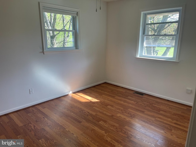 unfurnished room featuring baseboards, wood finished floors, and a healthy amount of sunlight