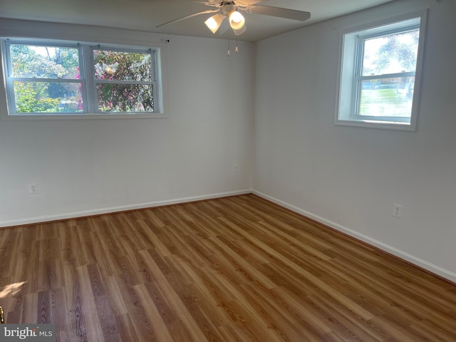 empty room with baseboards, ceiling fan, wood finished floors, and a healthy amount of sunlight