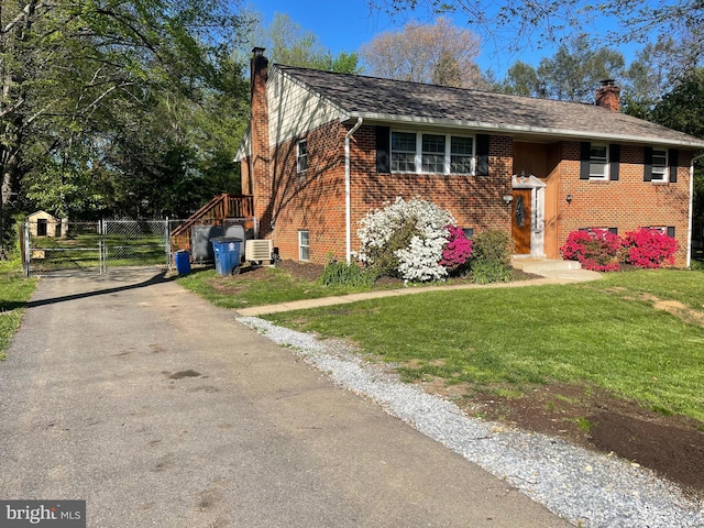 raised ranch featuring a gate, a chimney, a front yard, and brick siding