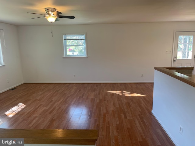 interior space with baseboards, a ceiling fan, wood finished floors, and a wealth of natural light