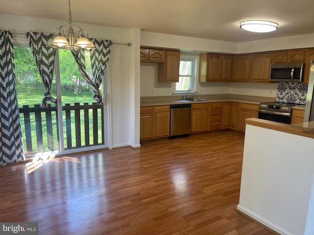 kitchen with decorative light fixtures, appliances with stainless steel finishes, wood finished floors, a sink, and a notable chandelier