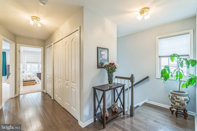 hallway featuring baseboards, an upstairs landing, and dark wood-type flooring