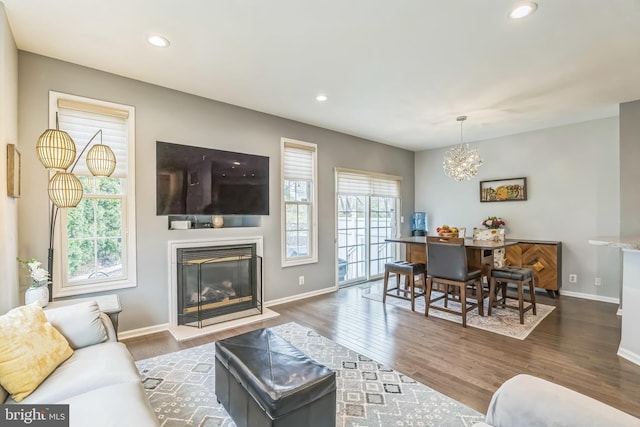 living room featuring a chandelier, baseboards, wood finished floors, and a glass covered fireplace