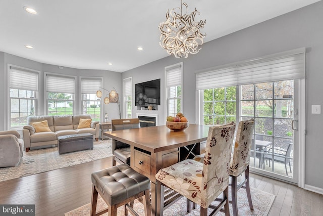 dining area with recessed lighting, an inviting chandelier, a glass covered fireplace, and light wood-style floors
