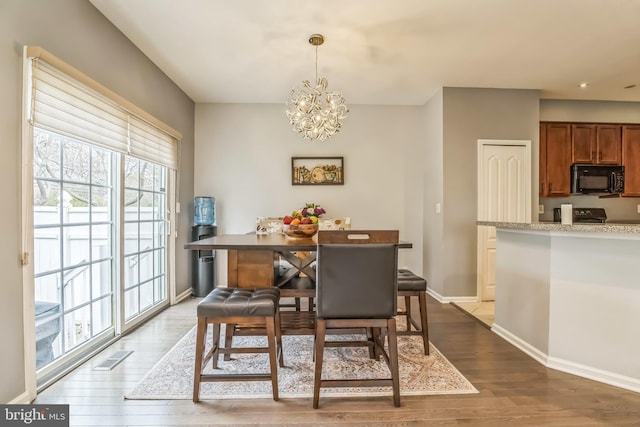 dining room with dark wood-type flooring, plenty of natural light, a notable chandelier, and baseboards