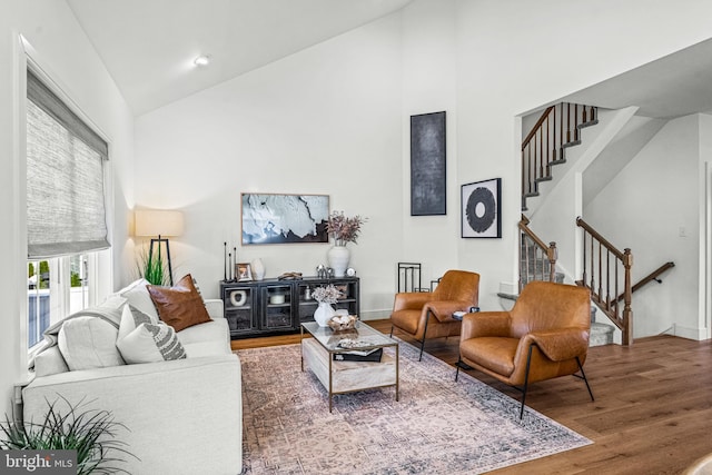 living area with stairs, high vaulted ceiling, wood finished floors, and baseboards