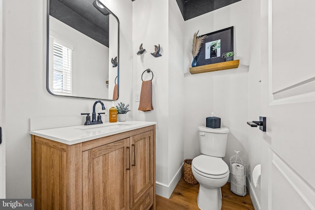 bathroom with toilet, vanity, wood finished floors, and baseboards