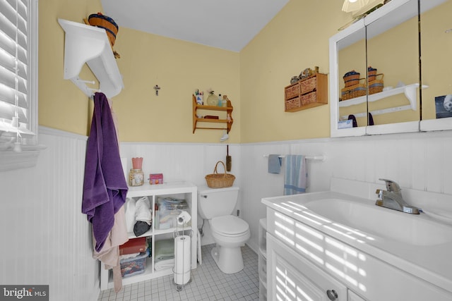 half bathroom with vanity, toilet, tile patterned flooring, and a wainscoted wall